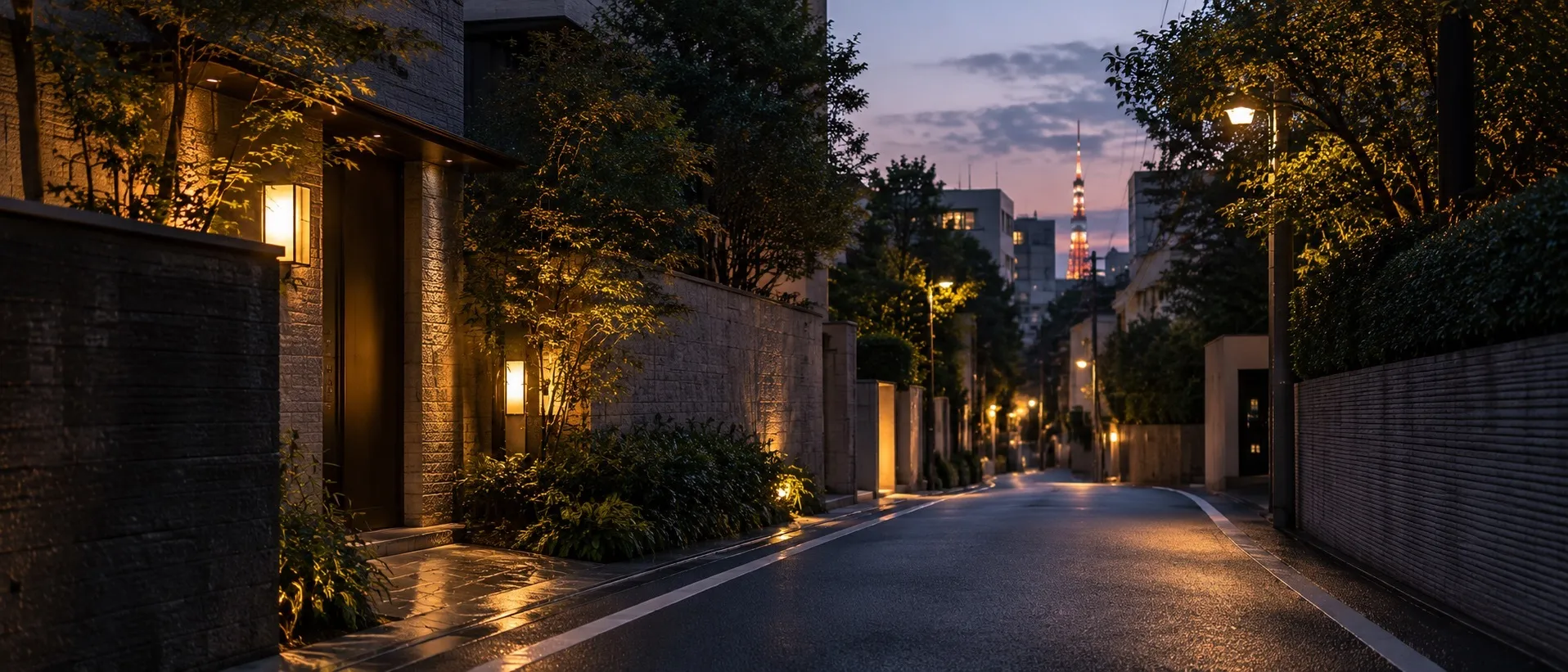 A quiet residential street in Azabu at dusk, stone walls and entrance lamps lit, Tokyo Tower rising beyond the trees