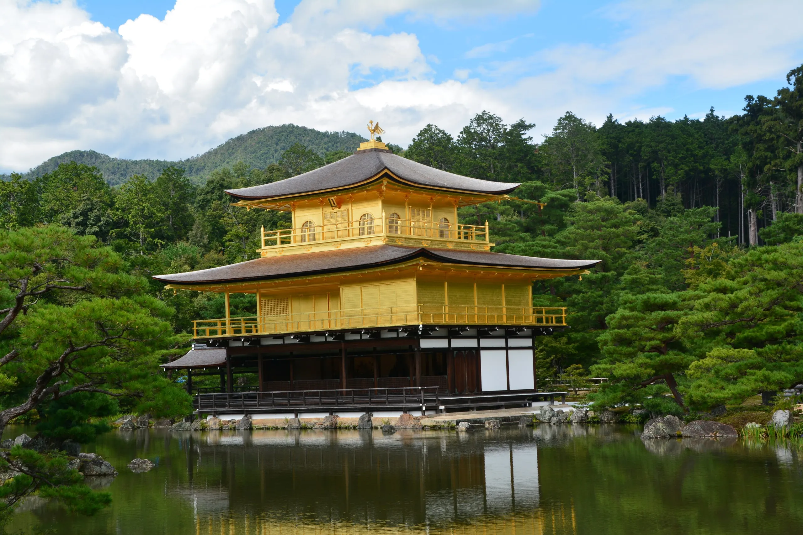 Kinkaku-ji, the Golden Pavilion, reflected in its still pond against forested hills