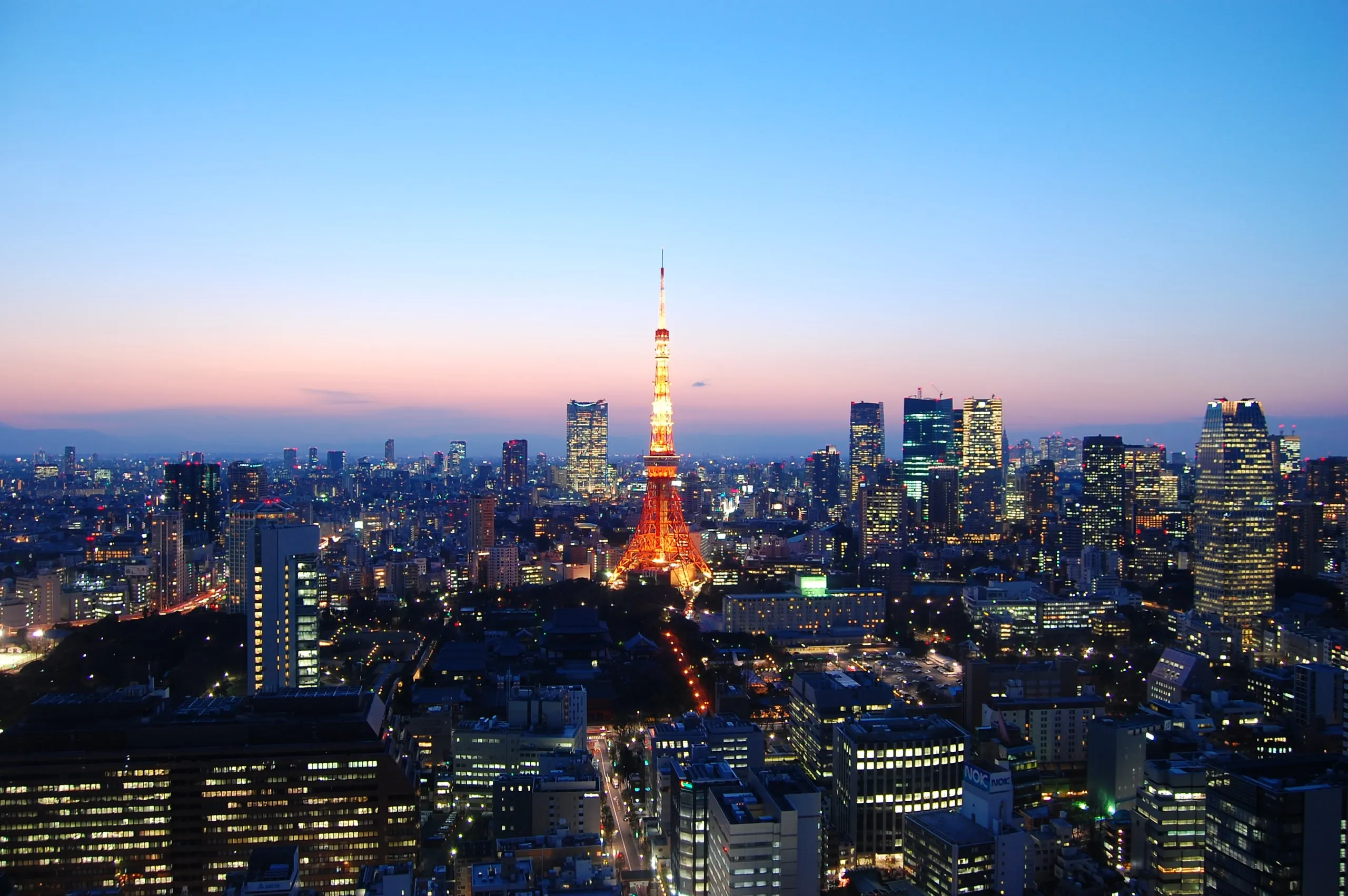 Tokyo Tower standing lit above the city at dusk, the sky fading from rose to deep blue
